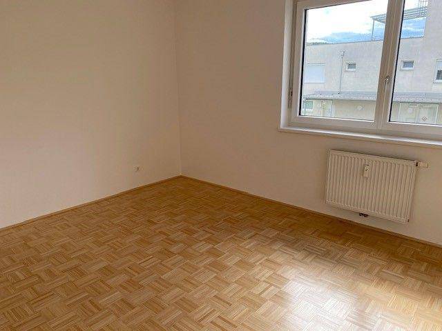 Helles Schlafzimmer mit Parkettboden und großem Fenster, bietet einen angenehmen Rückzugsort.
