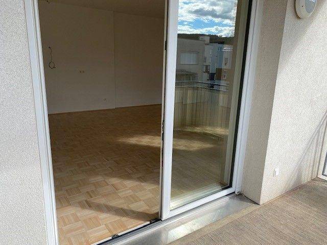 Blick vom Balkon in einen hellen Wohnraum mit Parkettboden und großen Schiebetüren.