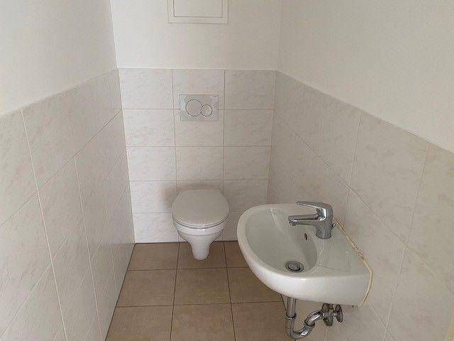 Separates WC mit wandhängender Toilette und kleinem Handwaschbecken, hell gefliest.
