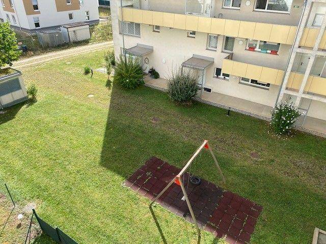 Gemeinschaftlicher Gartenbereich mit Rasenfläche und einem Spielgerät für Kinder.