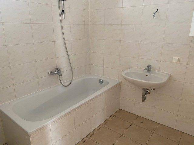 Badezimmer mit Badewanne, Waschbecken und hellen Fliesen, funktional und gepflegt.