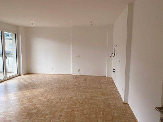 Heller Wohnbereich mit Parkettboden und weißen Wänden, bietet viel Platz für individuelle Einrichtung.