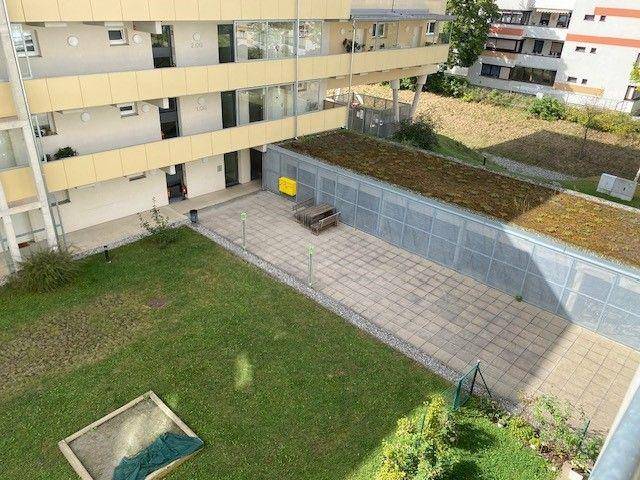 Innenhof mit Rasenfläche, Sandkasten und gepflastertem Bereich, umgeben von Gebäuden.