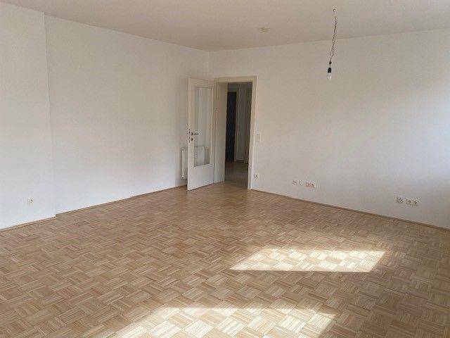 Leerer Wohnraum mit Parkettboden und viel Tageslicht, bereit für neue Bewohner.