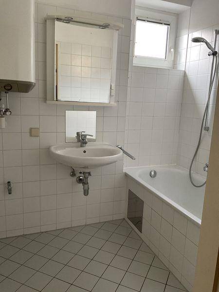Badezimmer mit weißen Fliesen, Waschbecken und einer Badewanne unter dem Fenster.