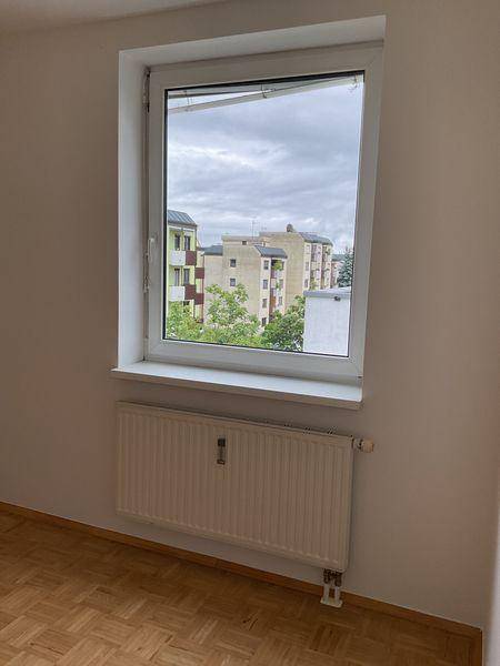 Schlafzimmer mit Parkettboden und Fenster, das einen Blick auf die umliegenden Gebäude bietet.