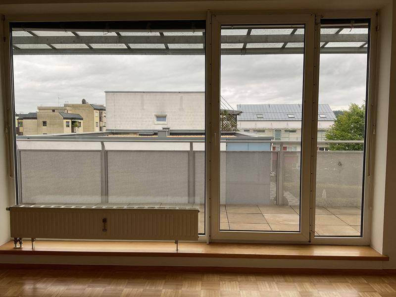 Leeres Wohnzimmer mit Parkettboden und großem Fenster mit Zugang zur Terrasse.