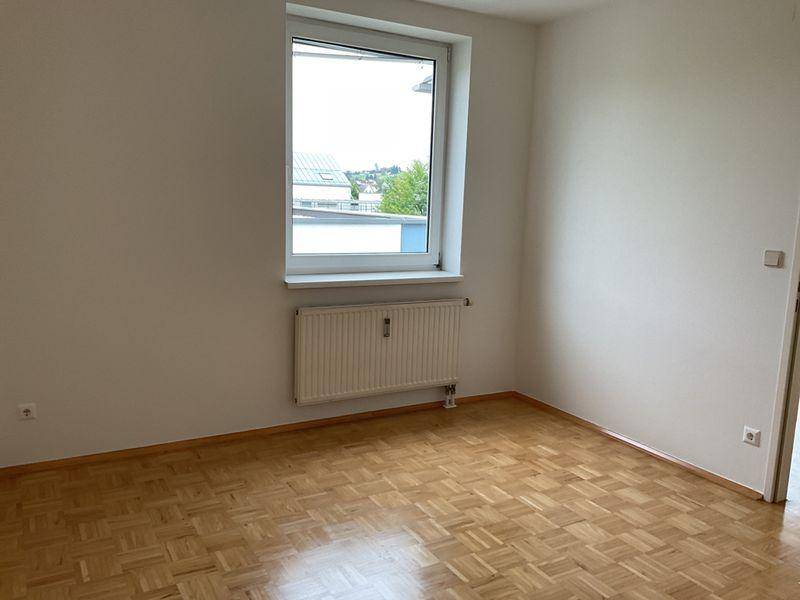 Helles Schlafzimmer mit Parkettboden und großem Fenster, das viel Licht spendet.
