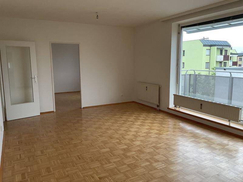 Wohnzimmer mit Parkettboden und großem Fenster, das viel Tageslicht hereinlässt.