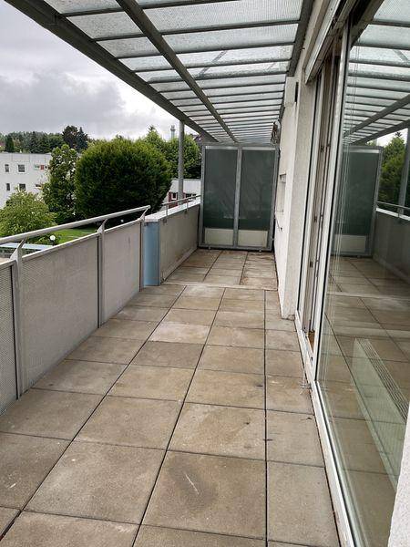 Geräumige geflieste Terrasse mit Überdachung und Metallgeländer, umgeben von Bäumen.