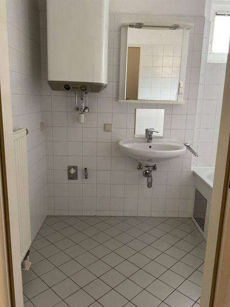 Einfaches Badezimmer mit weißen Fliesen, Waschbecken und Warmwasserboiler.