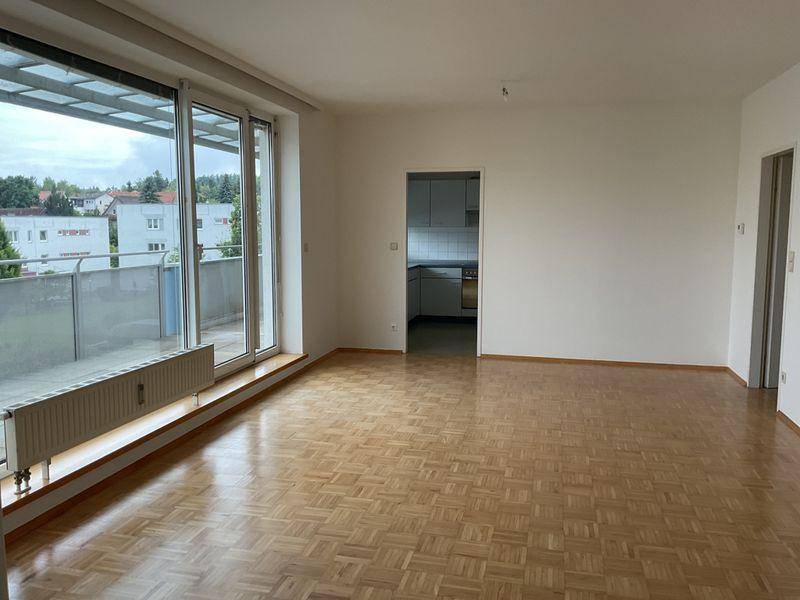 Helles Wohnzimmer mit Parkettboden und Blick auf die separate Küche.