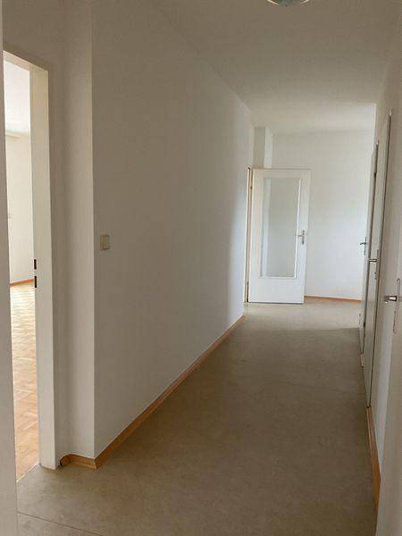 Heller Flur mit schlichten weißen Wänden und Vinylboden, führt zu weiteren Räumen.