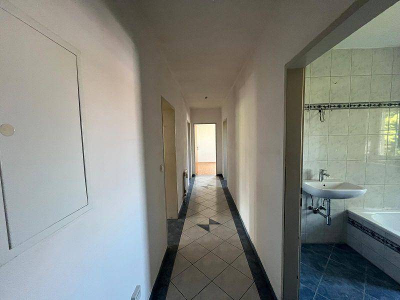 Langer Flur mit Fliesenboden, der zu einem Badezimmer mit blauen Fliesen führt.