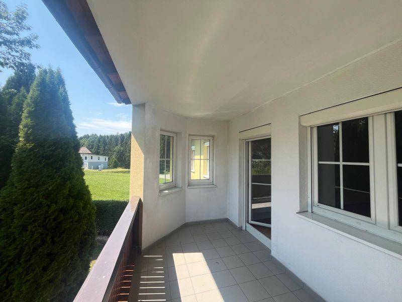 Heller Balkon mit Fliesenboden und Blick auf die grüne Landschaft und ein weiteres Gebäude.