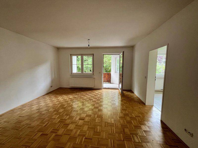 Helles Wohnzimmer mit Parkettboden und direktem Zugang zu einem kleinen Balkon.