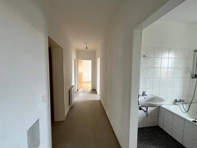 Langer Flur mit Zugang zu einem Badezimmer, ausgestattet mit Badewanne und Waschbecken.