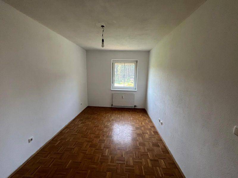 Helles Schlafzimmer mit Parkettboden und Fenster mit Blick ins Grüne.