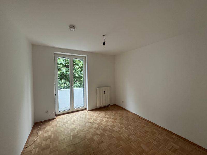 Helles Schlafzimmer mit Fischgrätparkett und großem Fenster mit Blick ins Grüne.