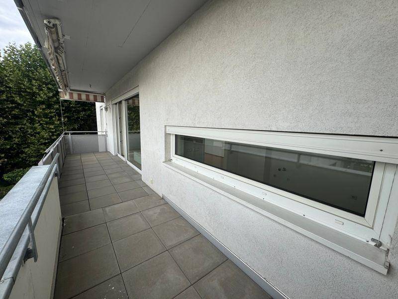 Langer Balkon mit grauen Fliesen und Blick ins Grüne, ausgestattet mit Markise.