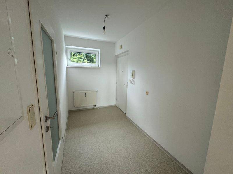 Eingangsbereich mit hellem Boden, kleinem Fenster und Heizkörper, wirkt einladend.