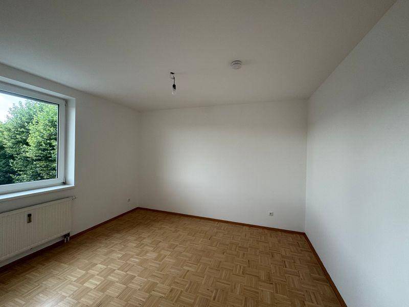 Ruhiges Schlafzimmer mit Parkettboden, großem Fenster und Heizkörper, bietet Grünblick.