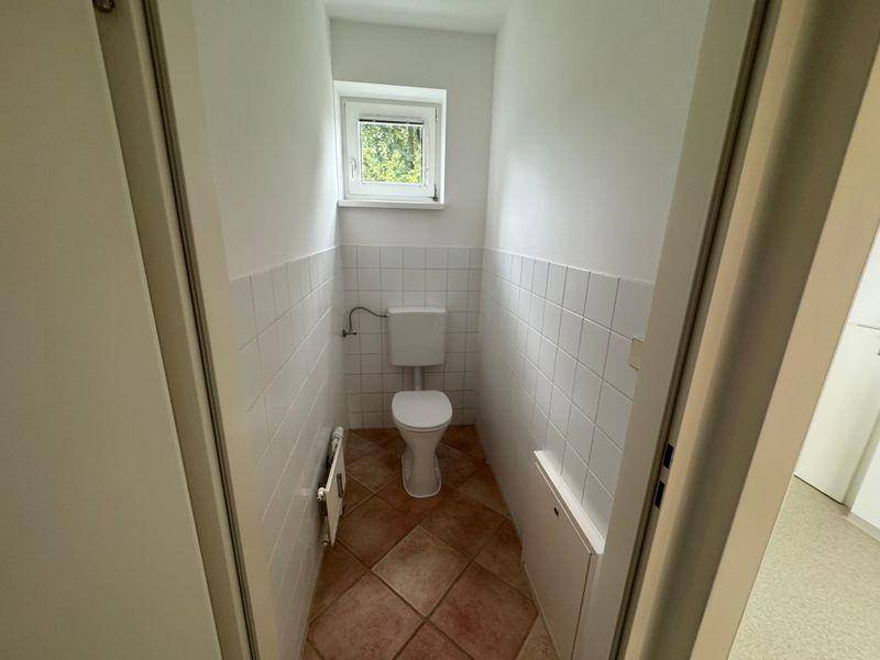 Separates WC mit Toilette, gefliesten Wänden und kleinem Fenster, funktional gestaltet.