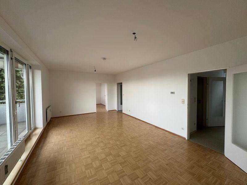 Geräumiges Wohnzimmer mit Parkettboden und großen Fenstern zum Balkon, sehr hell.