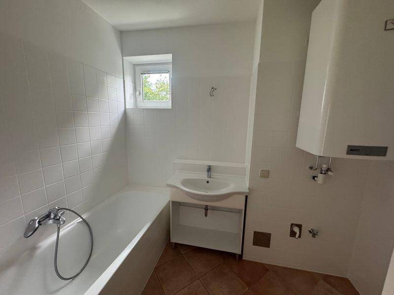 Helles Badezimmer mit Badewanne, Waschbecken und Warmwasserbereiter, gefliest.