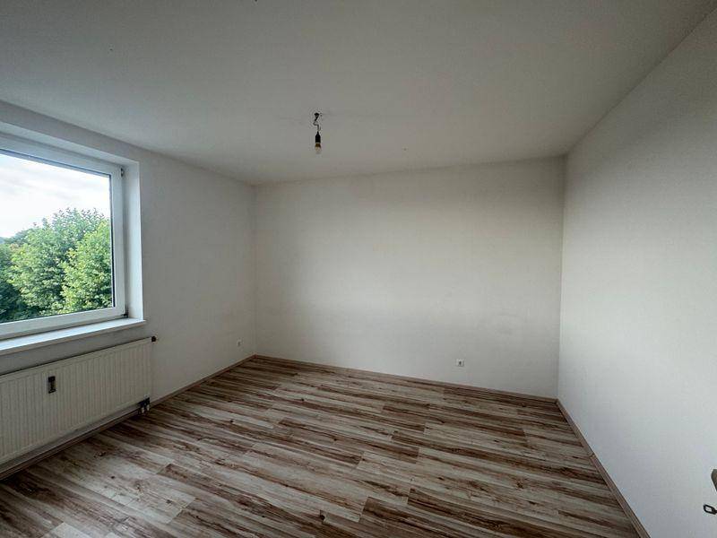 Helles Zimmer mit Laminatboden und großem Fenster, das einen schönen Blick ins Grüne bietet.