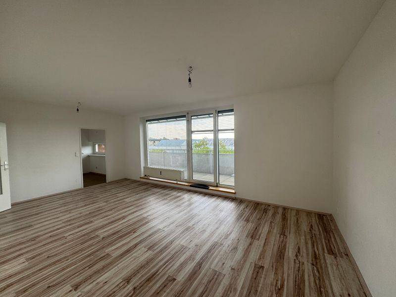 Geräumiges Wohnzimmer mit Laminatboden und großem Fenster, das Zugang zum Balkon bietet.
