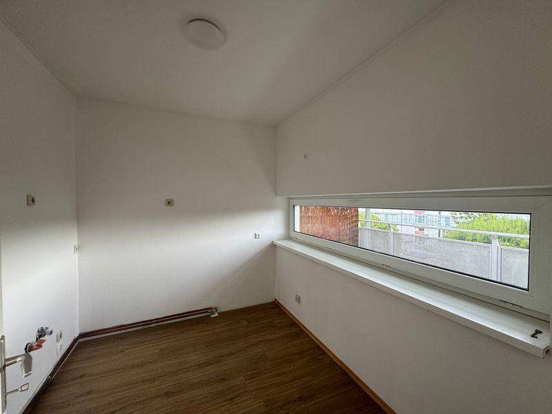 Helles Zimmer mit Laminatboden und einem breiten, niedrigen Fenster, ideal als Schlaf- oder Arbeitszimmer.