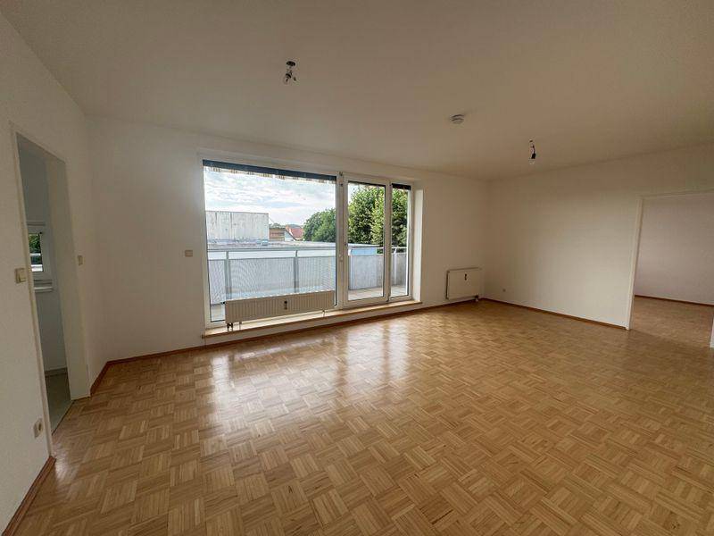 Großzügiges Wohnzimmer mit Parkett und viel Tageslicht durch die breite Fensterfront.
