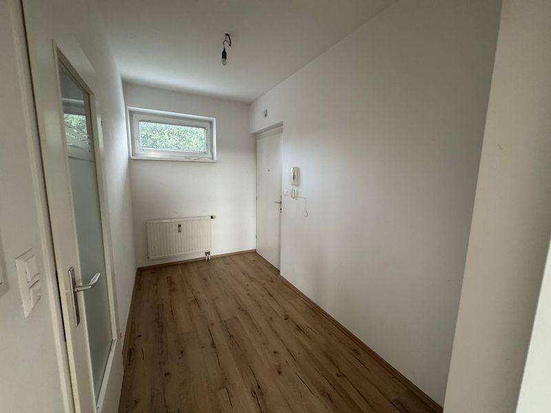Heller Flur mit Laminatboden, kleinem Fenster und Gegensprechanlage neben der Eingangstür.