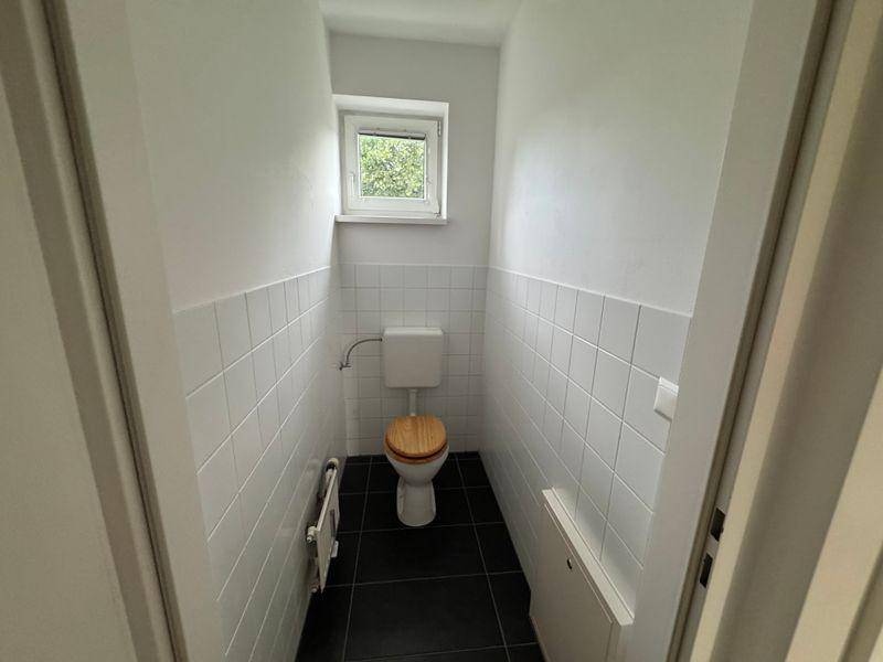 Kleines Gäste-WC mit Toilette, Fliesenboden und einem Fenster für natürliche Belüftung.