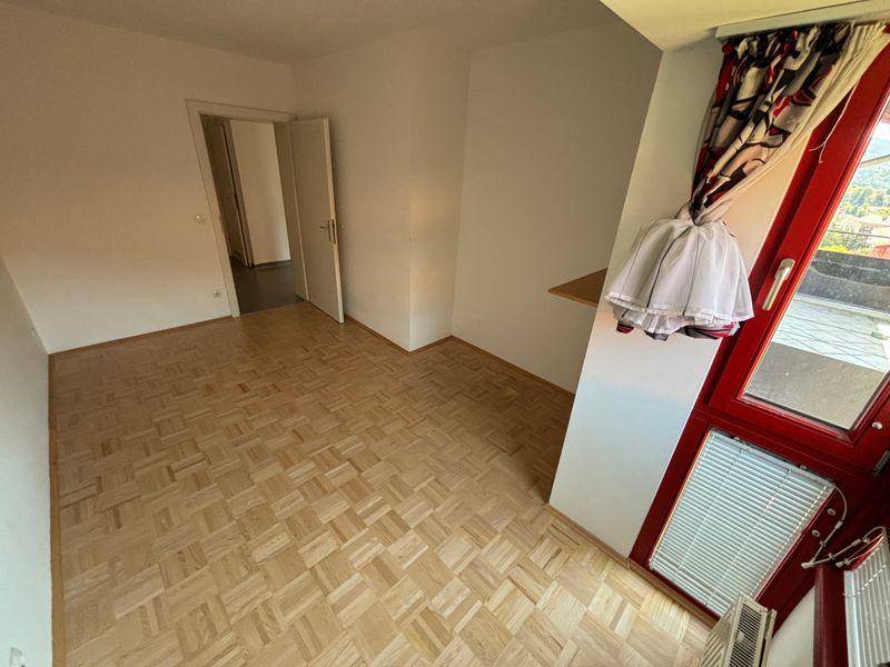 Geräumiges Schlafzimmer mit Parkettboden, weiß gestrichenen Wänden und Zugang zum Balkon.