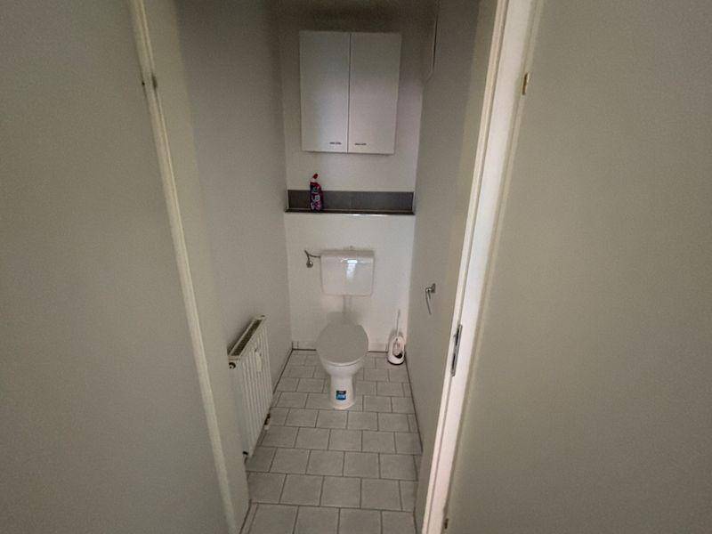 Separates WC mit Toilette, Heizkörper und hellen Fliesen am Boden.