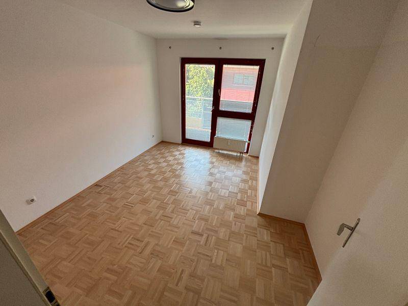 Helles Schlafzimmer mit Parkettboden und großer Fensterfront, die viel Tageslicht hereinlässt.