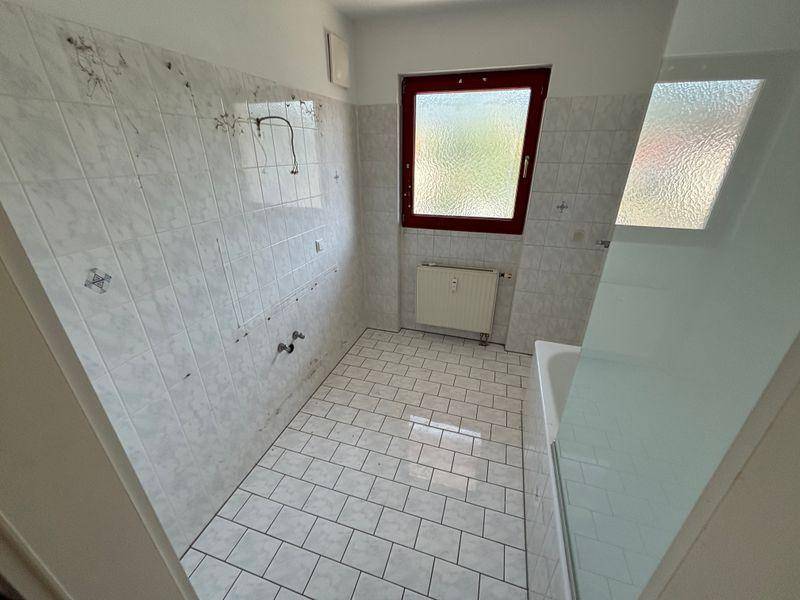 Badezimmer in Renovierungszustand mit weißen Fliesen an Wänden und Boden sowie einem Fenster.