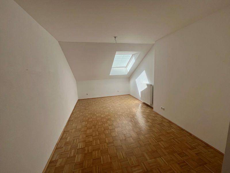 Helles Zimmer im Dachgeschoss mit Parkettboden, weißen Wänden und Dachfenster.