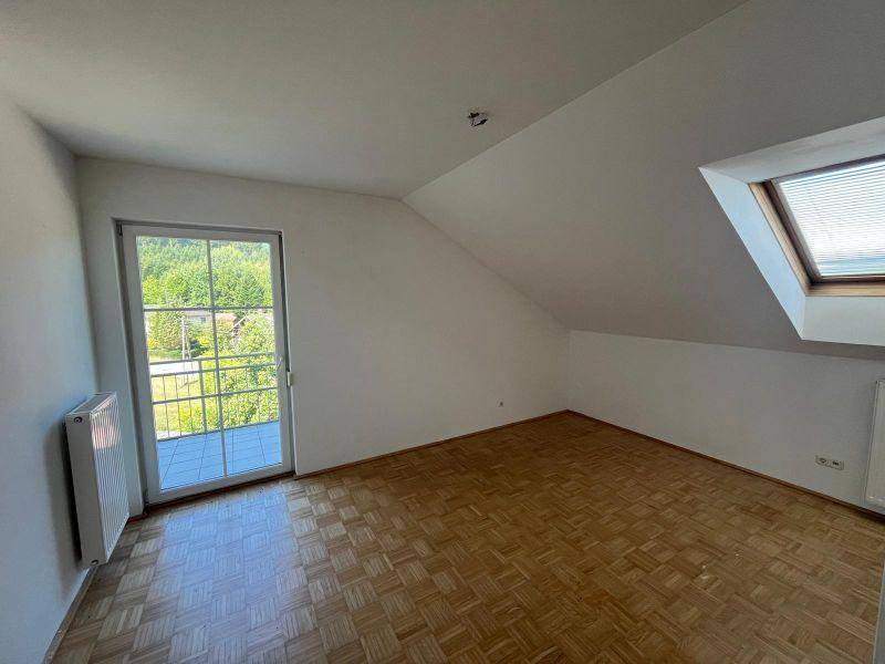 Lichtdurchflutetes Zimmer mit Parkettboden, Dachschräge und Zugang zum Balkon.