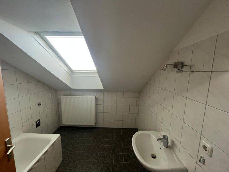 Helles Badezimmer im Dachgeschoss mit Badewanne, Waschbecken und Dachfenster.