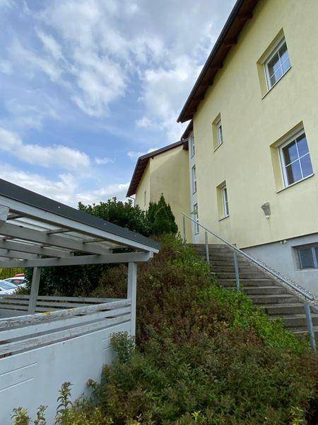 Außenansicht der Wohnanlage mit Carport, Treppenaufgang und umliegender Vegetation.