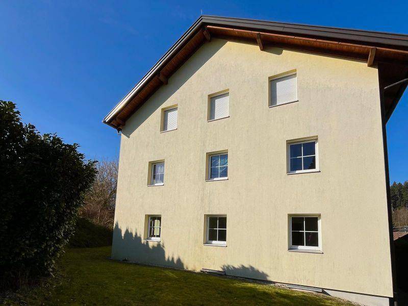 Seitenansicht eines Mehrfamilienhauses mit gelber Fassade und weißen Fenstern.