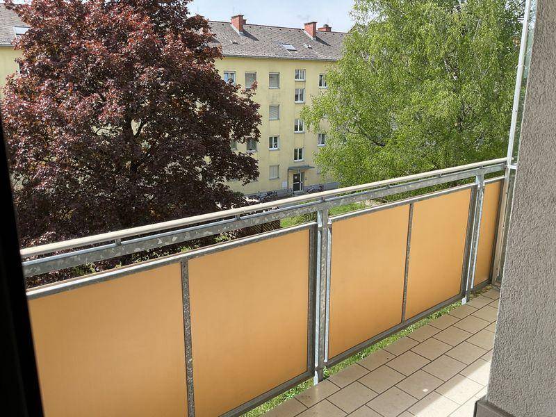 Balkon mit Fliesenboden und orangefarbenen Sichtschutzelementen, Blick auf Bäume und Nachbargebäude.