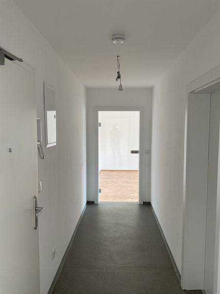 Heller Flur mit grauem Boden, Gegensprechanlage und Blick in einen angrenzenden Raum.
