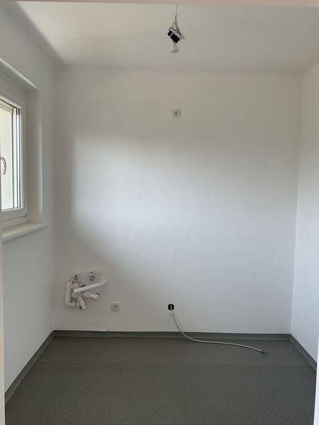 Leerer Raum mit grauem Boden und Fenster, vorbereitet für die Installation einer Küche.