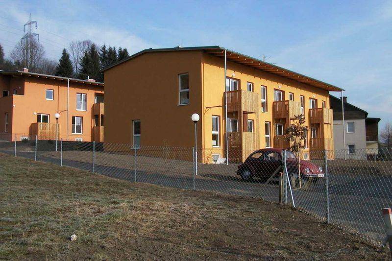 Mehrere Wohngebäude mit oranger Fassade, Balkonen und Blick auf die umliegende Landschaft.