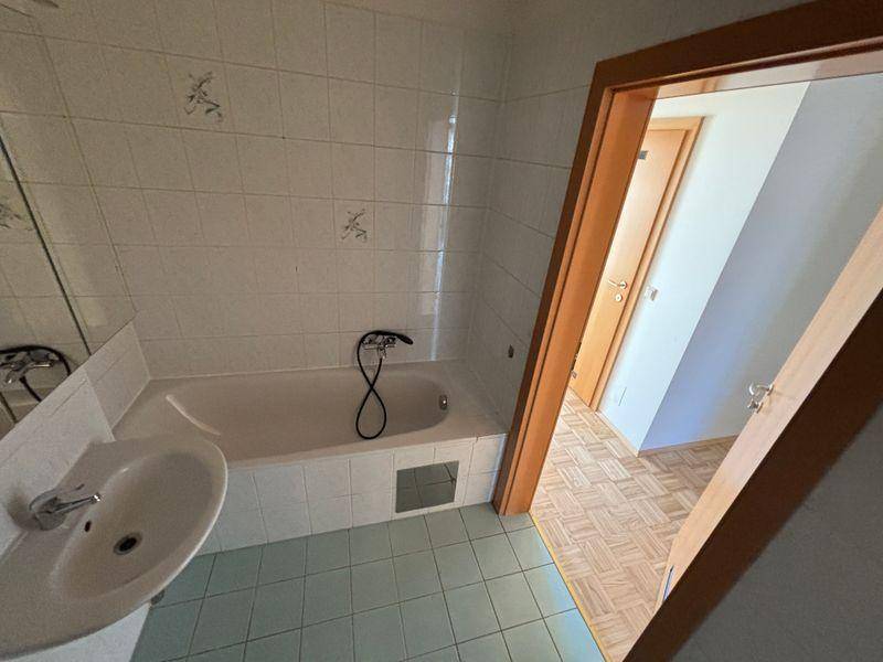 Badezimmer mit Badewanne, Waschbecken und hellblauen Bodenfliesen, praktisch und sauber.