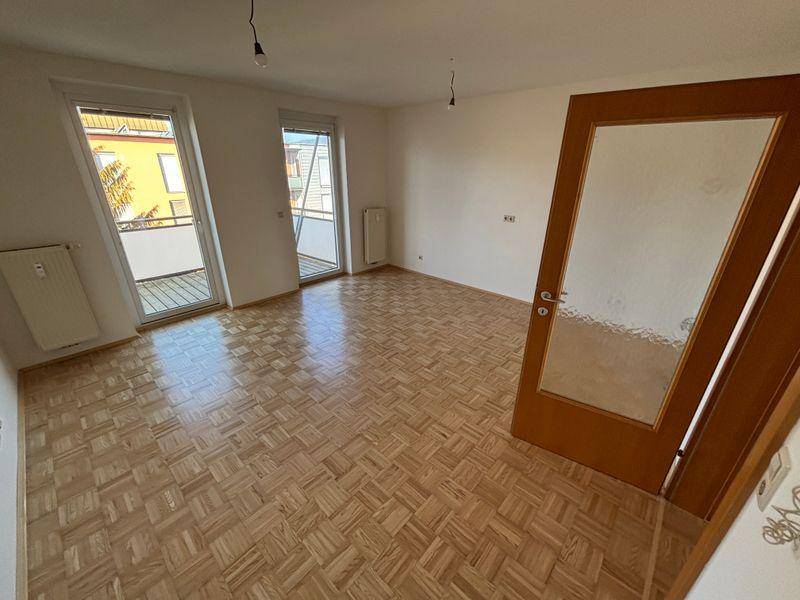 Helles Wohnzimmer mit Parkettboden und Zugang zu zwei Balkonen, ideal für natürliches Licht.